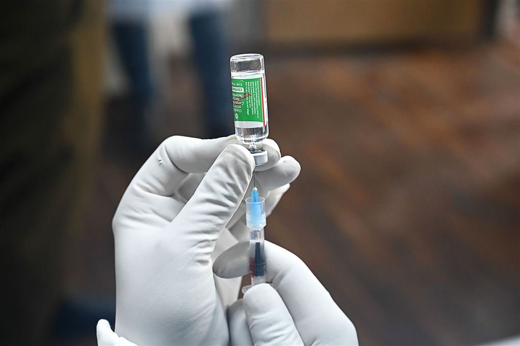En hånd med latexhandske trækker en vaccine dosis op i en kanyle. 