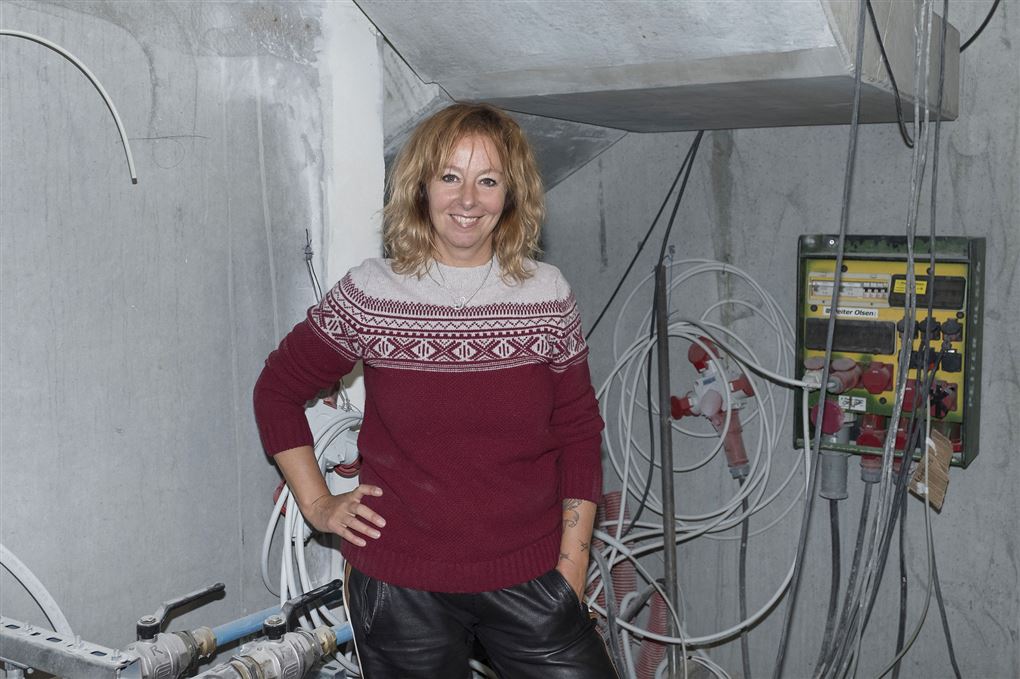 Puk Elgård iført en sweater hun står i et hus der ligner et renoveringsprojekt. 