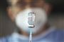 En vaccinedosis i forgrunden med en mand med mundbind bagefter