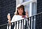 Joan Collins med et glas champagne i den ene hånd og peace-tegn med den anden på en altan. 