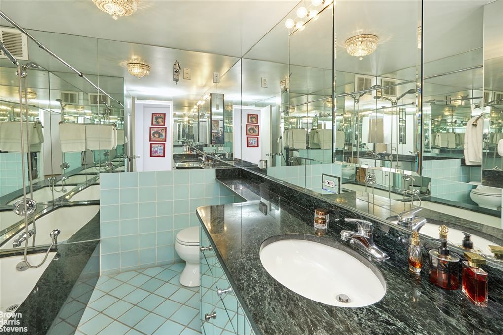 Et halv træt badeværelse med spejle over det hele og mintgrønne gulvfliser, der er lagt på skå. 