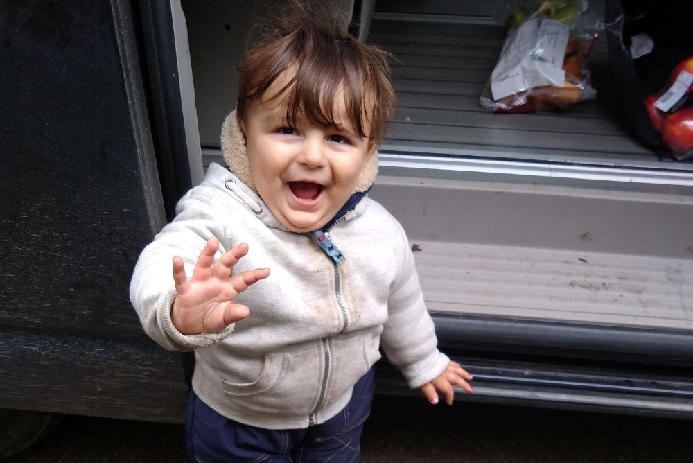 Billede af en smilende lille dreng der vinker mod kameraet