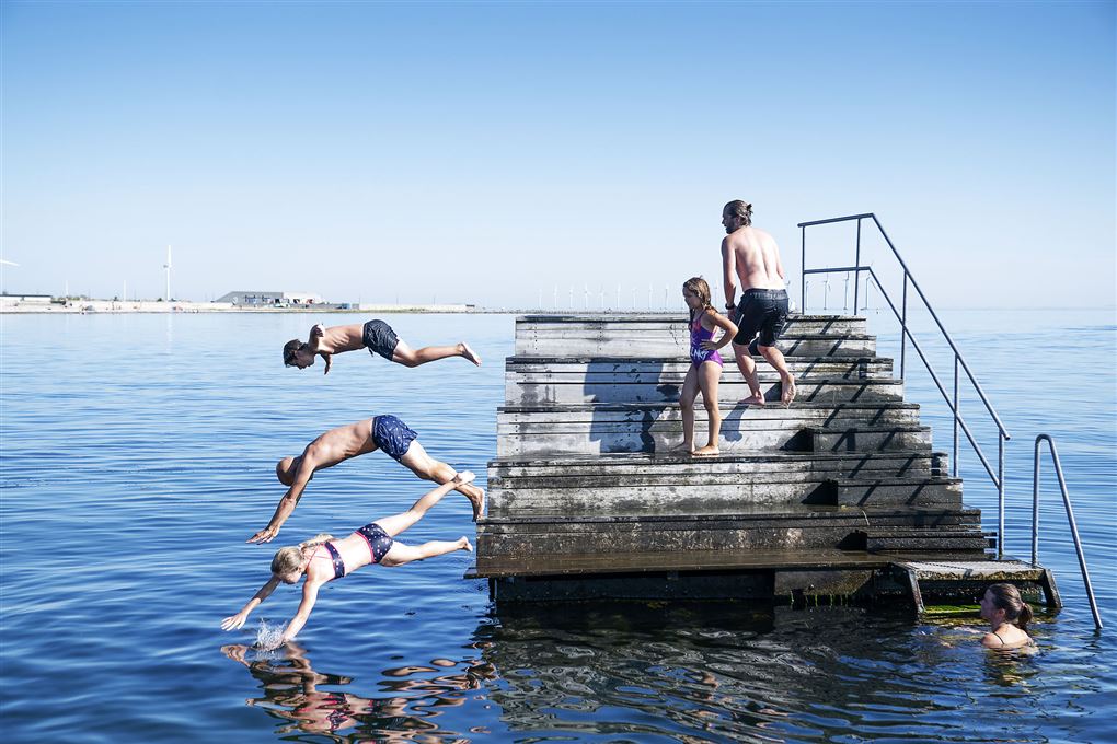 Voksne og børn hopper i vandet fra platform