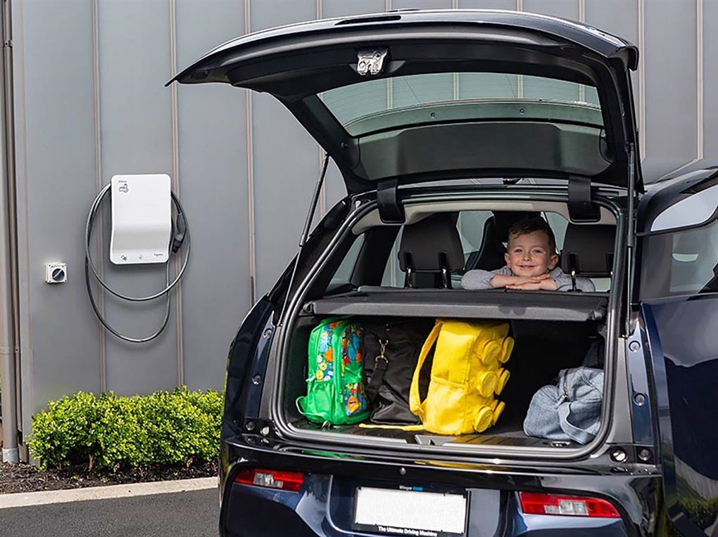 En lille dreng smiler og kigger ud af en bagsmæk på en bil