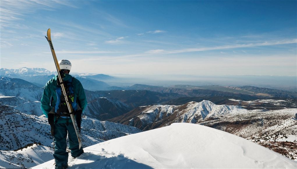 Mand med ski på ryggen på toppen af bjerg
