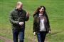 Prins William og Kate i jeans, sweatre og windbreaker jakker på en græsplæne. De griner. 