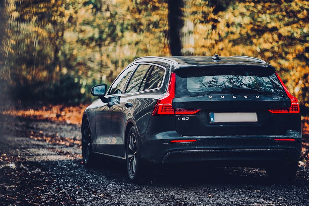 En mørkeblå Volvo V60 set bagfra i en skov med efterårsfarver.