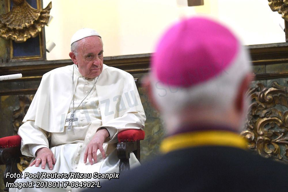 Pave Frans sidder på en trone foran ses en sløret katolsk præst. 