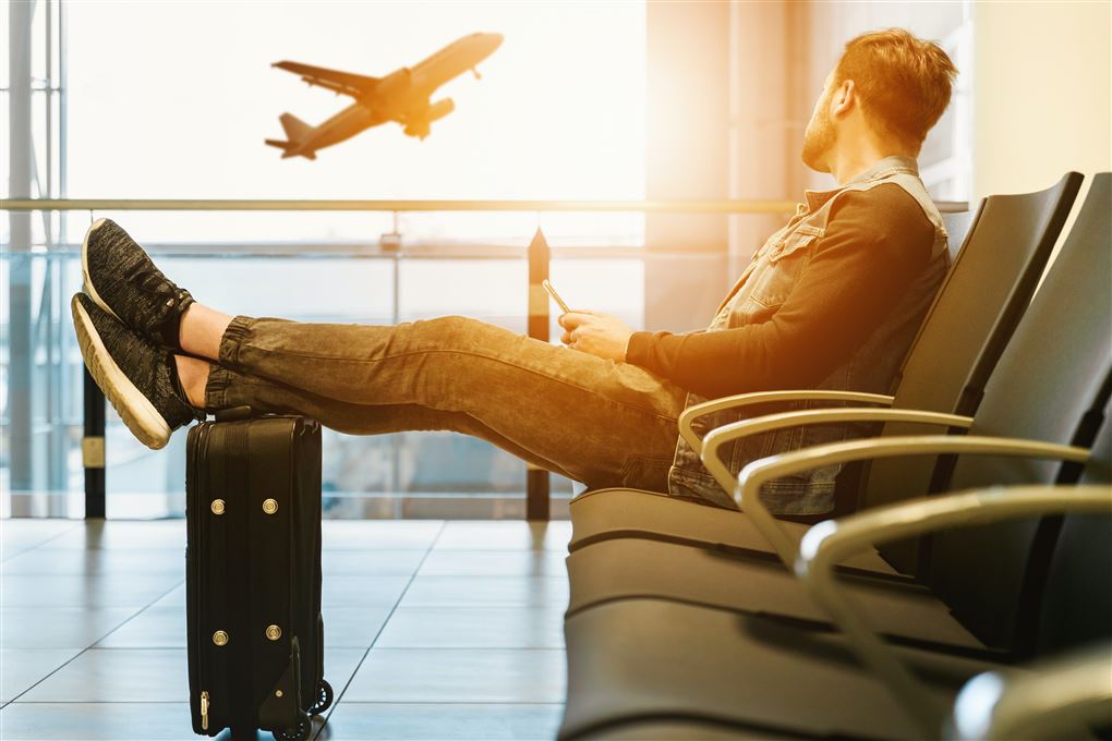 En mand sidder i en lufthavn med benene hvilende på en kuffert.