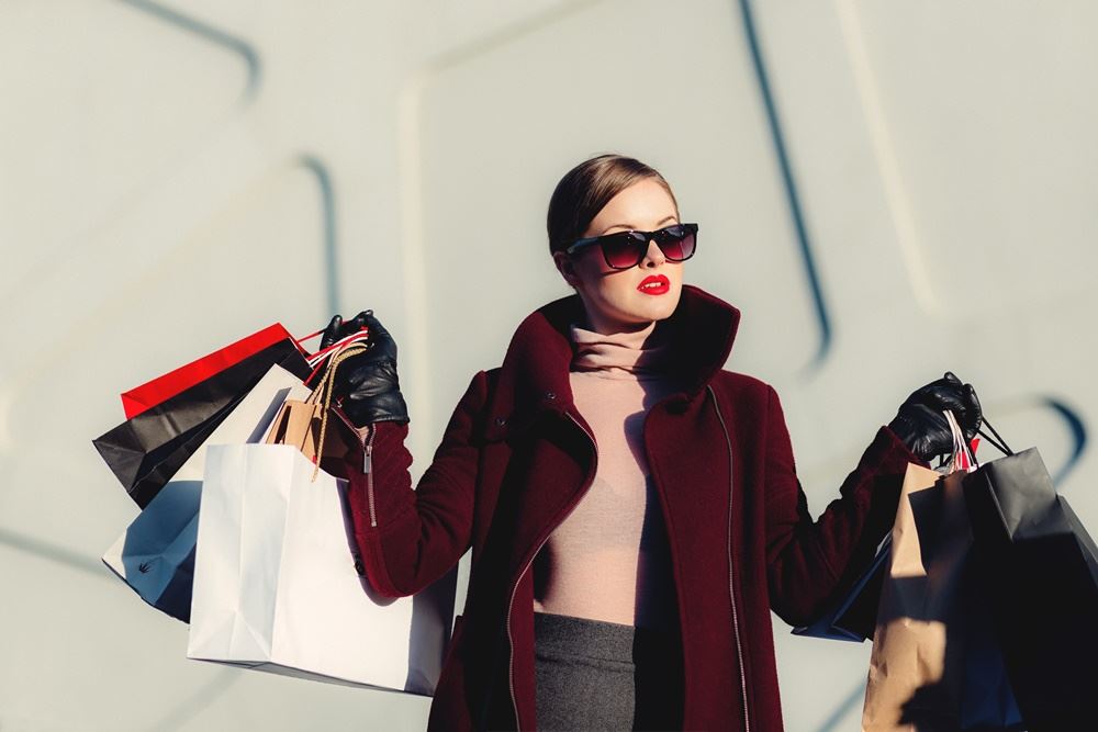 kvinde med solbriller står med indkøbsposer og tasker