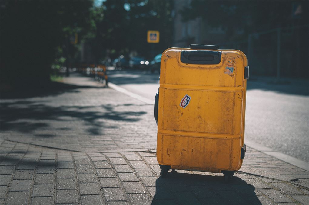 En gammel slidt gul kuffert står alene på et fortov.