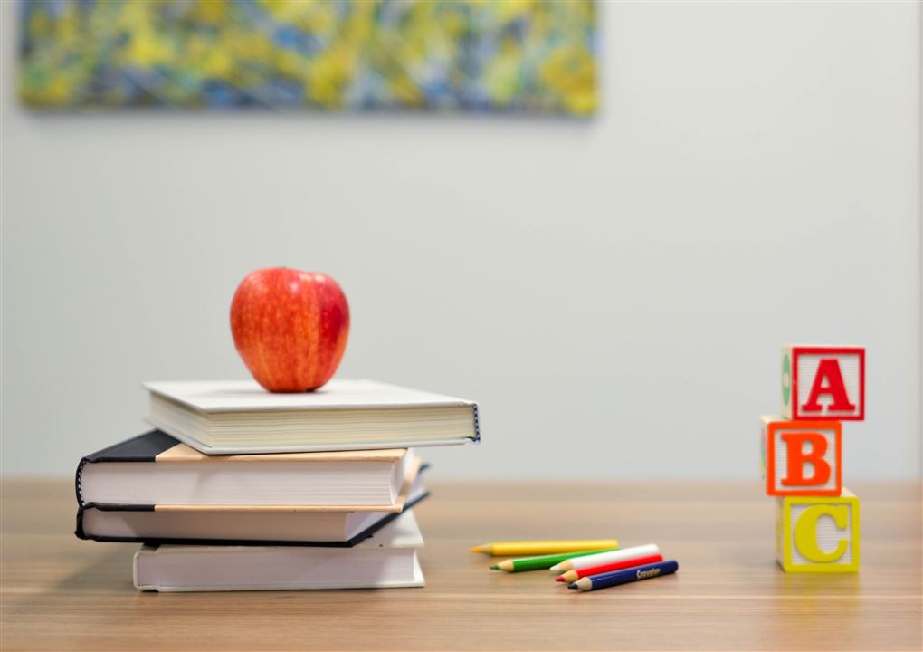 Et bord med bøger, blyanter, nogle bogstaver og et æble.
