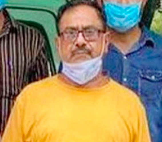 En mand i gul t-shirt og beskyttelsesmaske om halsen føres ud af politiet