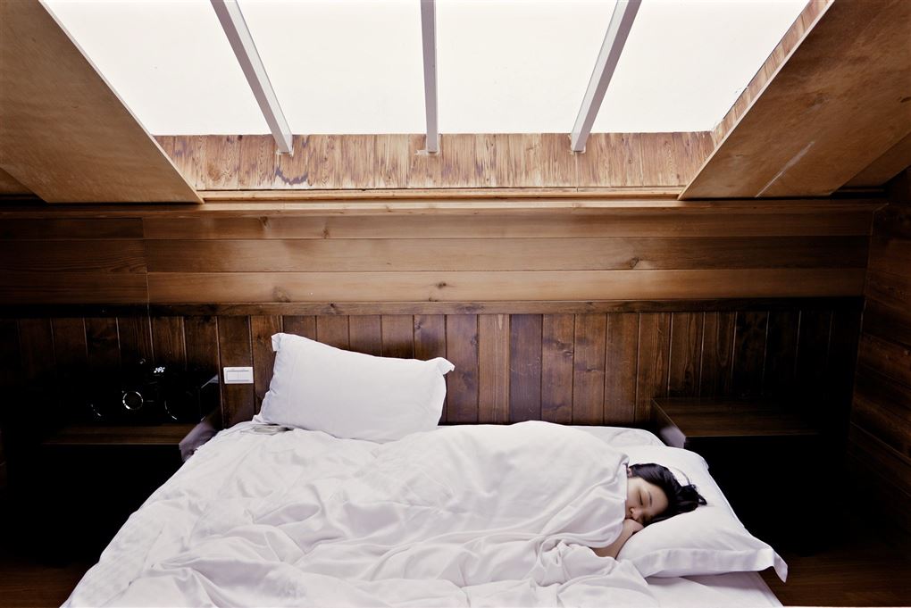 En sovende kvinde i en kæmpe seng med et ovenlysvindue over sig