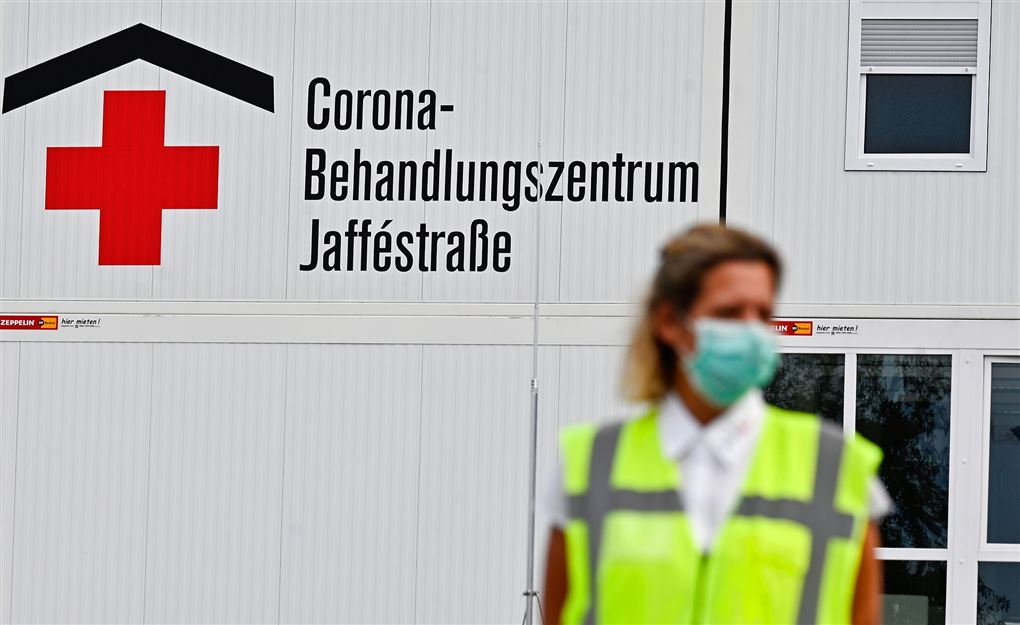 En hospitalsmedarbejder med maske på foran et corona-skilt