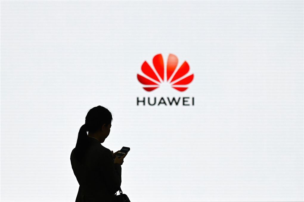 En silhouet af en kvinde med en mobiltelefon foran et stort Huawei-reklame