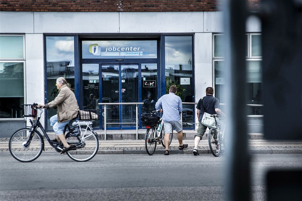 Et jobcenter med en cylende mand i forgrunden og to mænd som trækker deres cykler