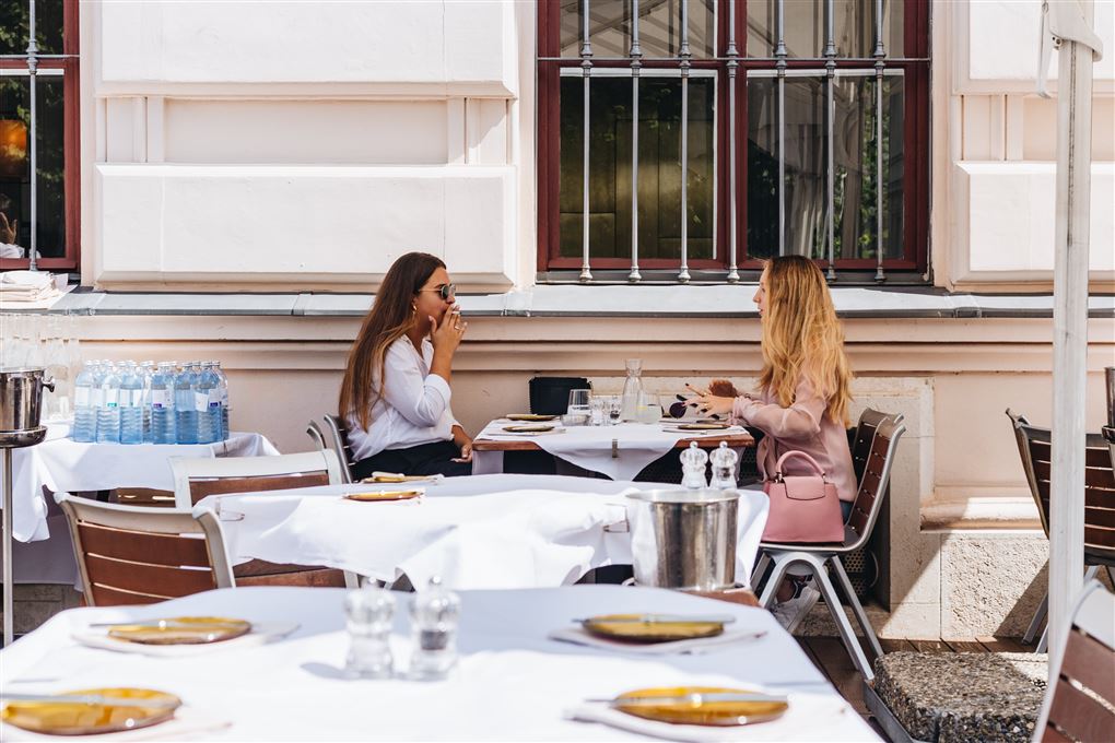 To kvinder hygger ved et bord og drikker kaffe med en stor smuk bygning i baggrunden