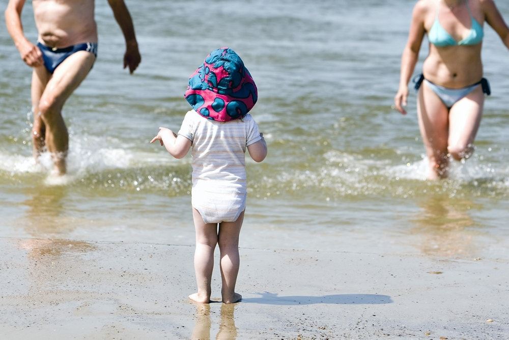 Et barn i sandet kigger ud på mor og far, der går ind fra vandet
