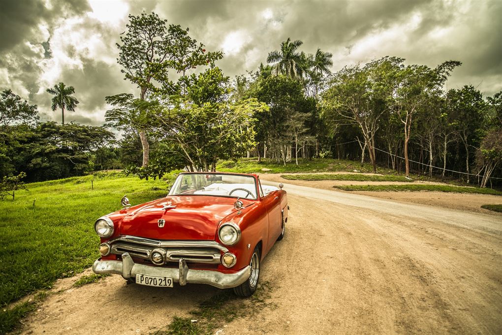 En gammel åben rød amerikanerbil uden for en jungle på Cuba