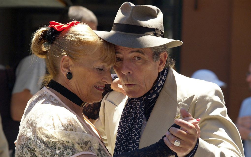 Et ældre par danser i solen - han har hat på og hun en rød sløjfe i håret
