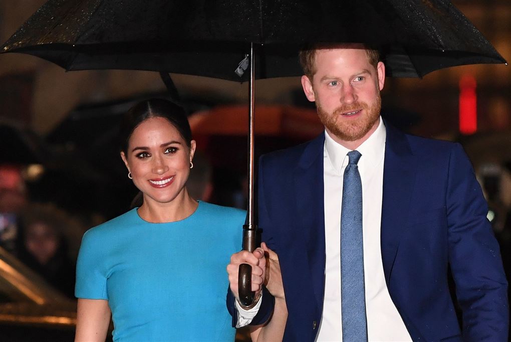 Meghan i en blå kjole og Harry i jakkesæt, som holder en paraply