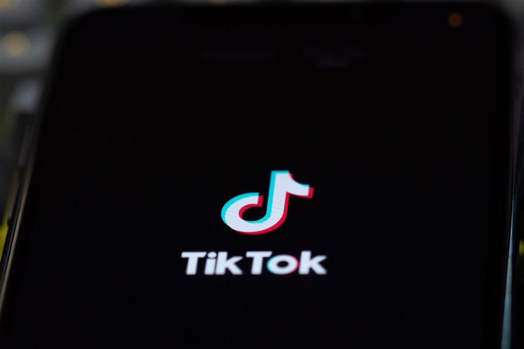 Billede af det sociale medie TikToks logo på en sort skærm med hvid skrift. Logoet ligner en node. 