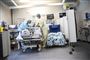 En hospitalsstue, hvor to læger eller sygesplejersker står ved en hospitalsseng med engangskitler, hårnet, handsker og masker på. 