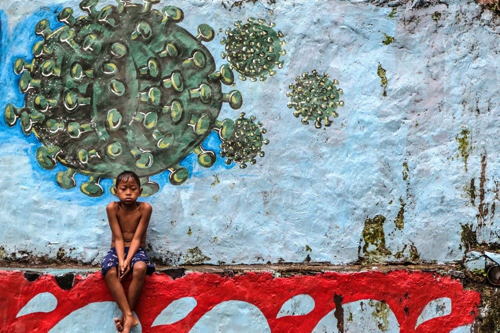 dreng sidder under et murmaleri der forestiller coronavirusset 