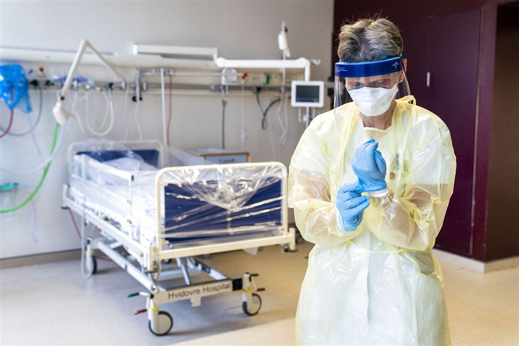 Sygeplejerske med maske og handsker står foran tom hospitalsseng
