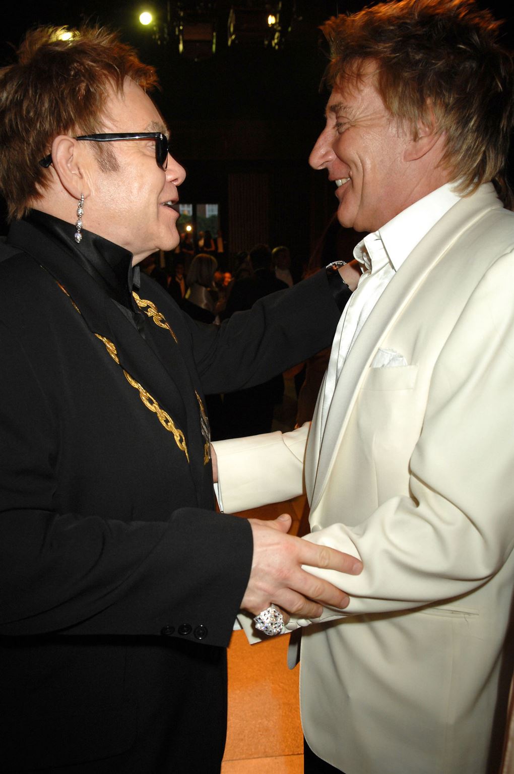 Elton John i mørket jakkesæt står og holder om Rod Stewart i hvidt jakkesæt.