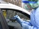 En person bliver testet for corona i sin bil af en person med handsker, engangskittel, visir, mundbind og hårnet på.