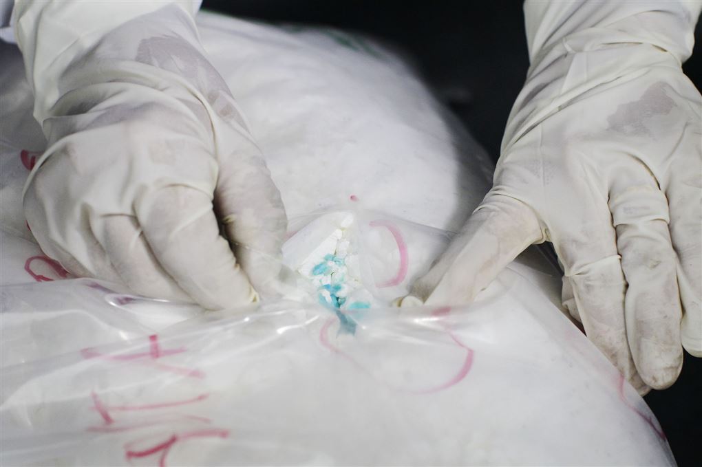 En stor pose med hvidt pulver bliver vist frem af et par hænder iført hvide latexhandsker