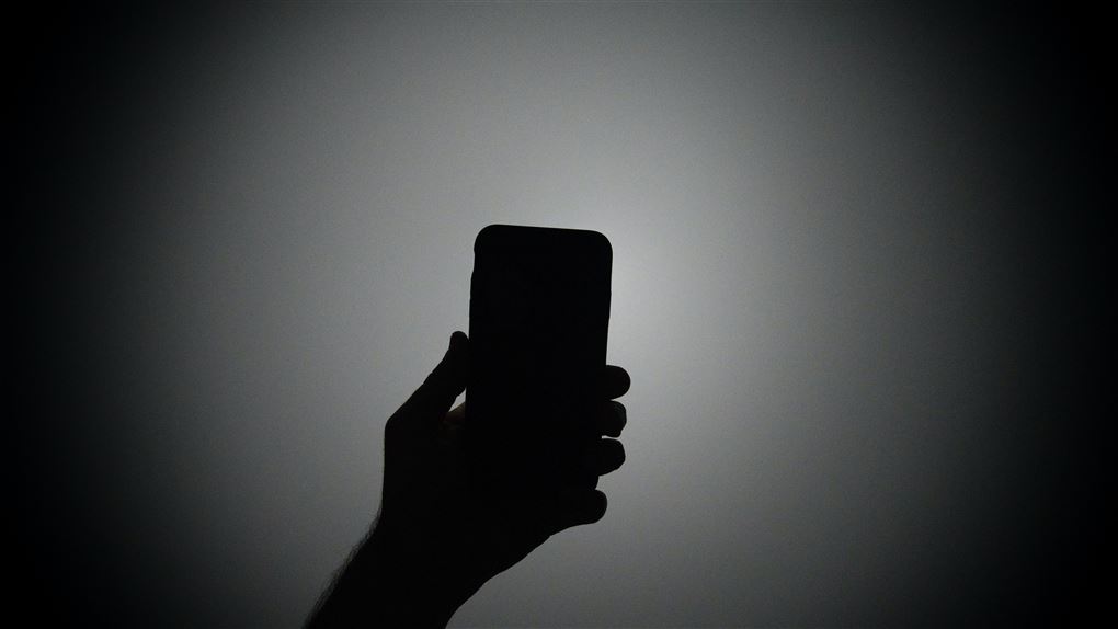En hånd holder en telefon som for at tage et billede af sige selv. Billedet er sort hvid. 