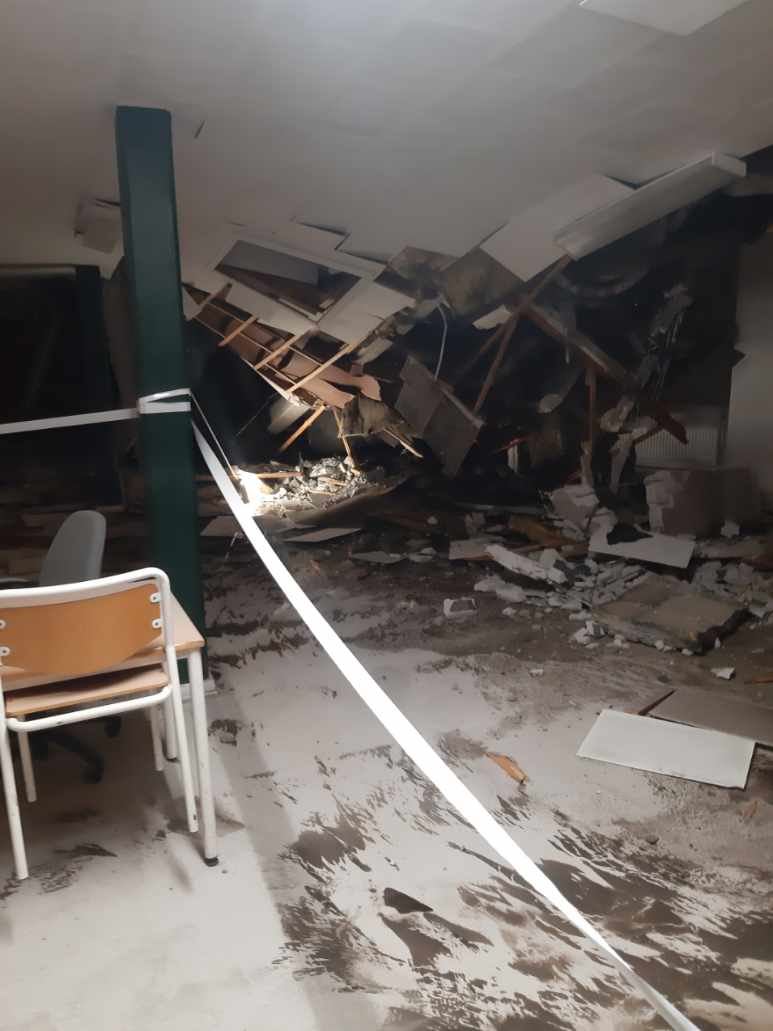 billede indefra bygningen, hvor loftet hænger og møbler er væltet omkuld.