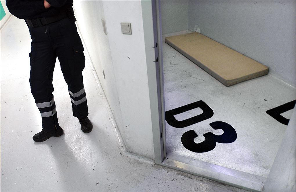 Detentionscelle med madras og en politimands fødder.