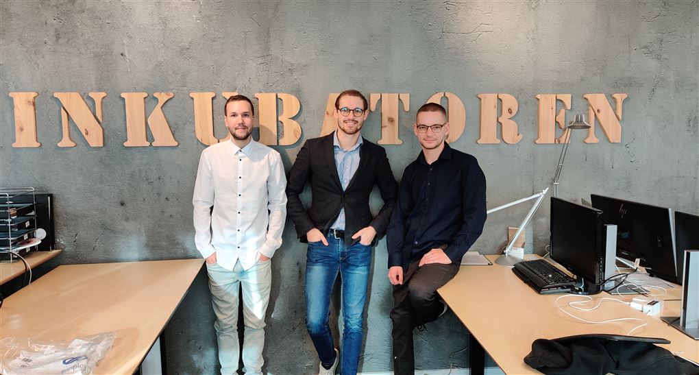 Tre unge mænd står op af en væg, hvor der står Inkubatoren