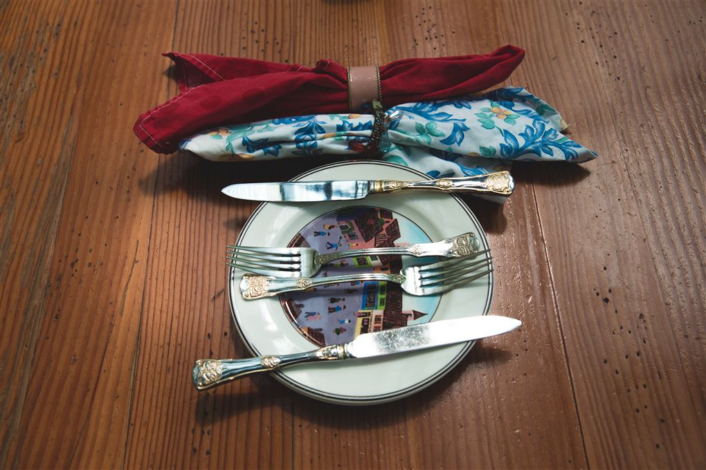 En tallerken med to gafler og to knive og to stofservietter foldet fint i servietringe.