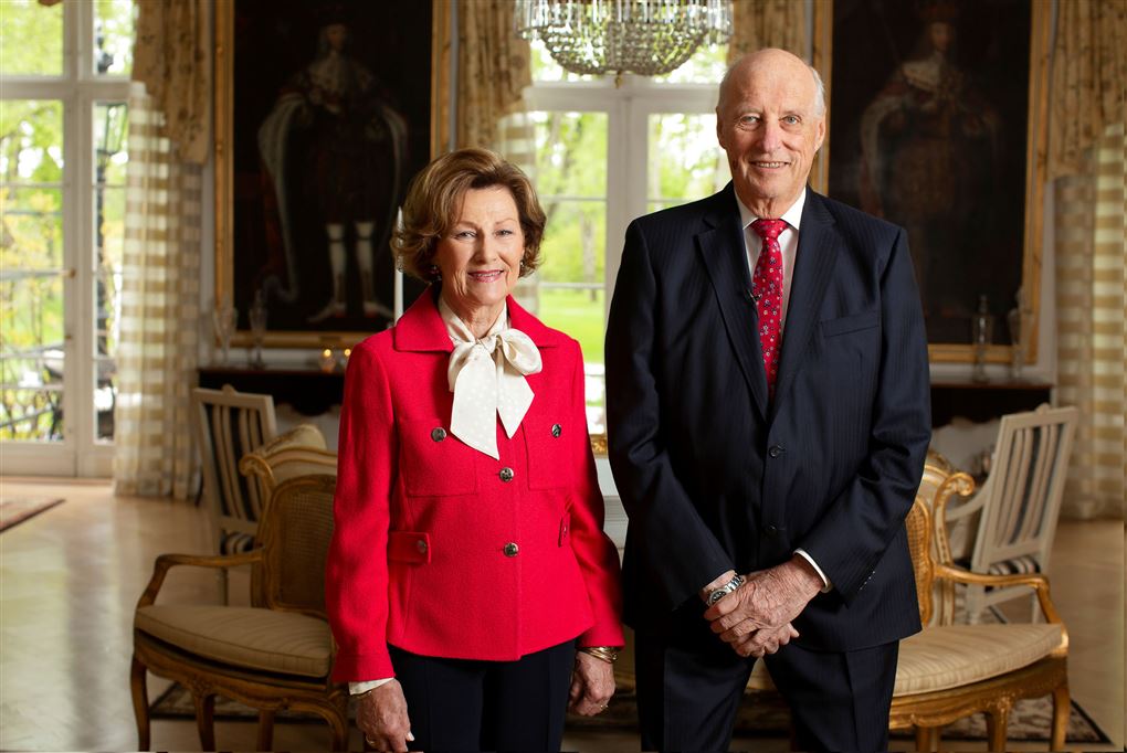 Portræt af dronning Sonja og kong Harald. Sonja er i en postkasserød blazer med en hvid skjorte under. Kongen er iført jakkesæt. 