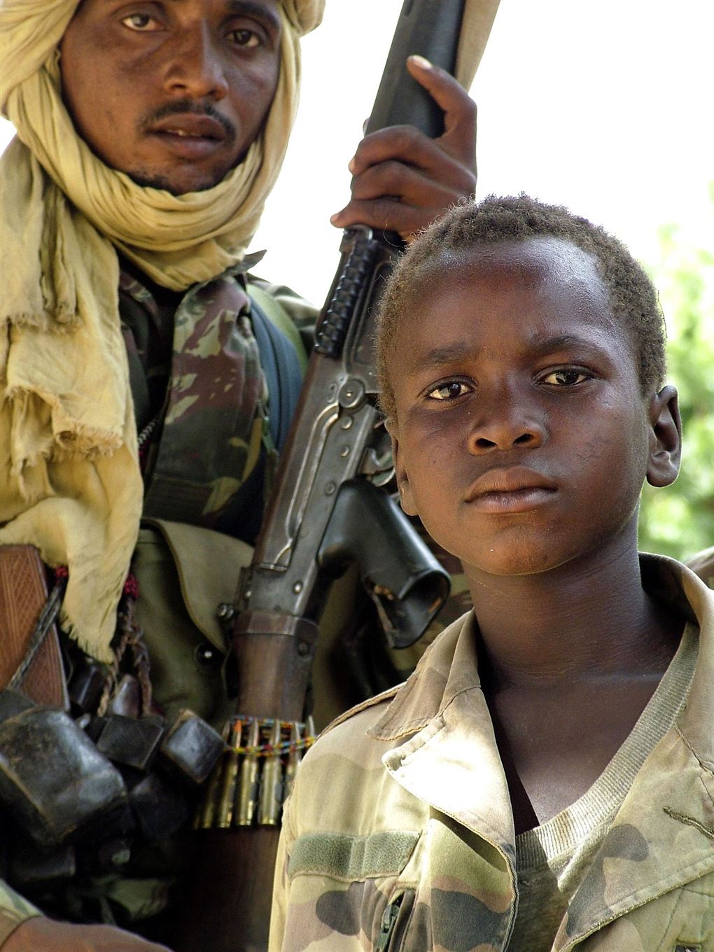 En ung dreng ved siden af en voksen soldat.