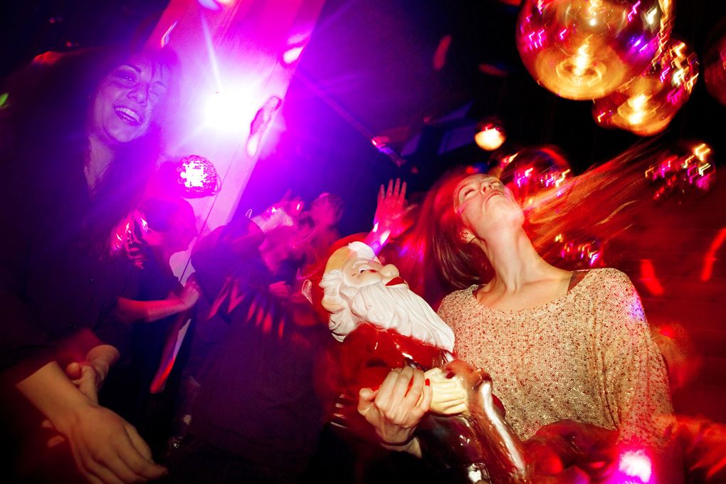 En kvinde danser på et diskotek med en havenisse på armen. Hun svinger med håret.