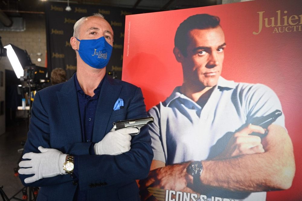 En mand står som James Bond med en pistol i hånden i baggrunden en plakat med Sean Connery
