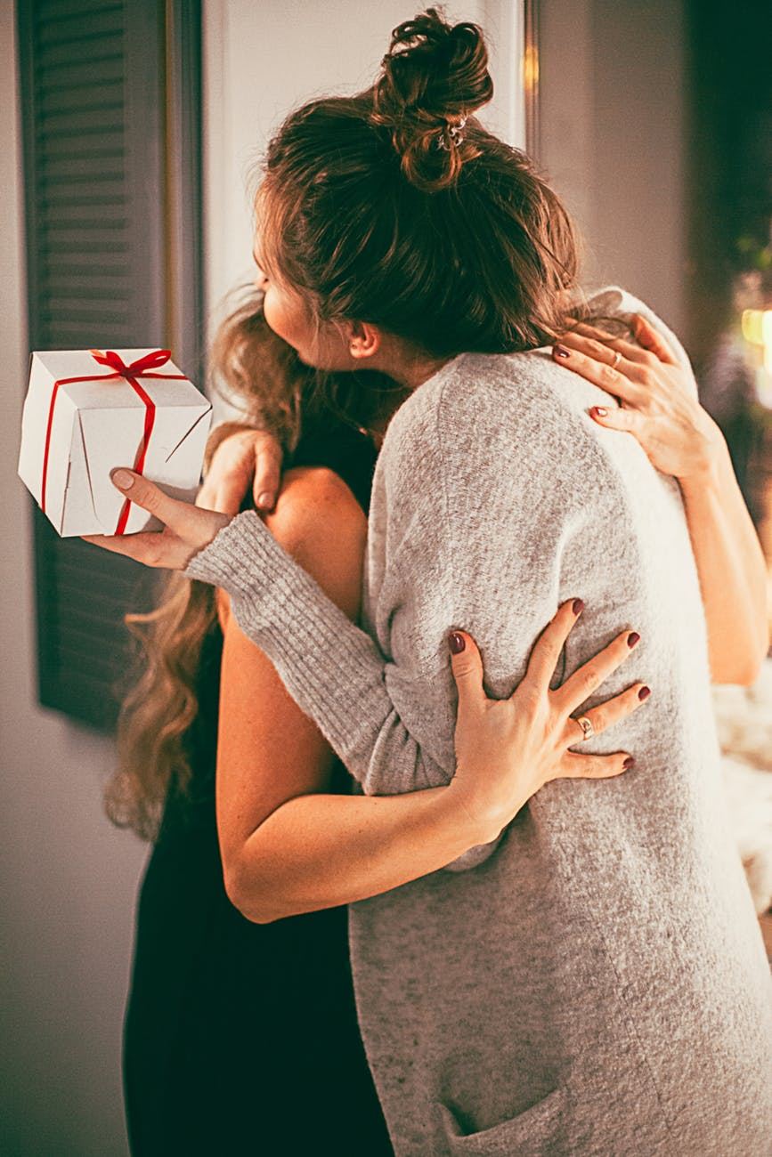 To unge kvinder giver hinanden et knus - den ene med en pakke i hånden