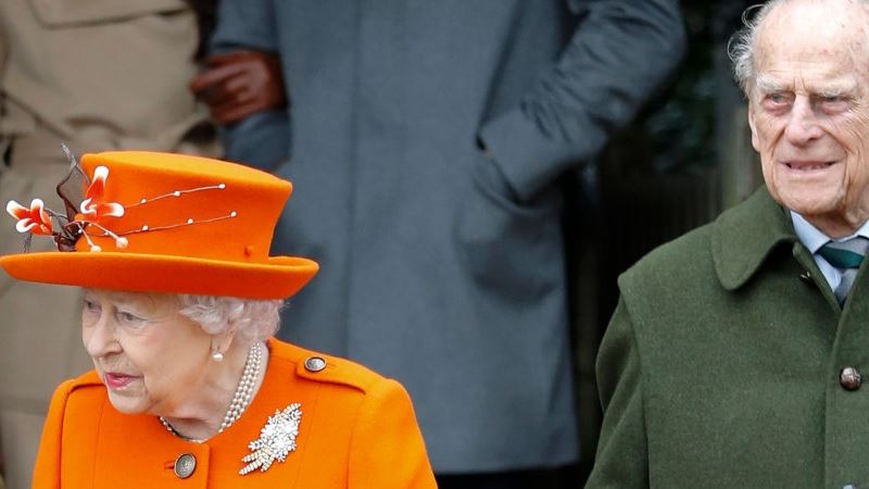 dronning elizabeth med orange hat sammen med sin mand prins hilip i grøn jakke