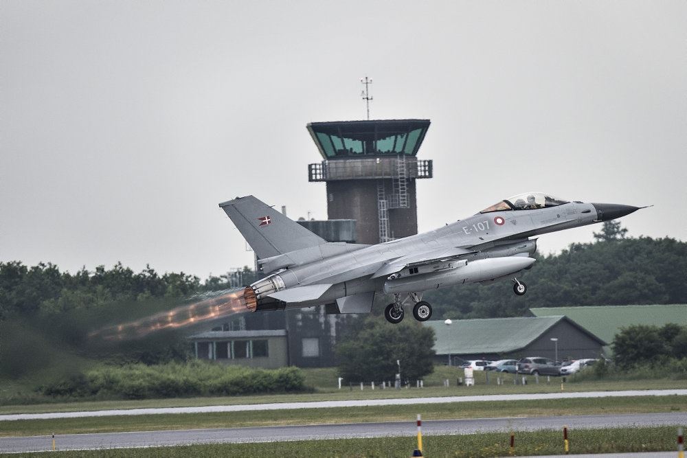 Et F16-fly letter med et kontroltårn i baggrunden