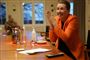 Mette Frederiksen jubler og klapper ved et stort mødebord i Marienborg. Hun har orange jakke på
