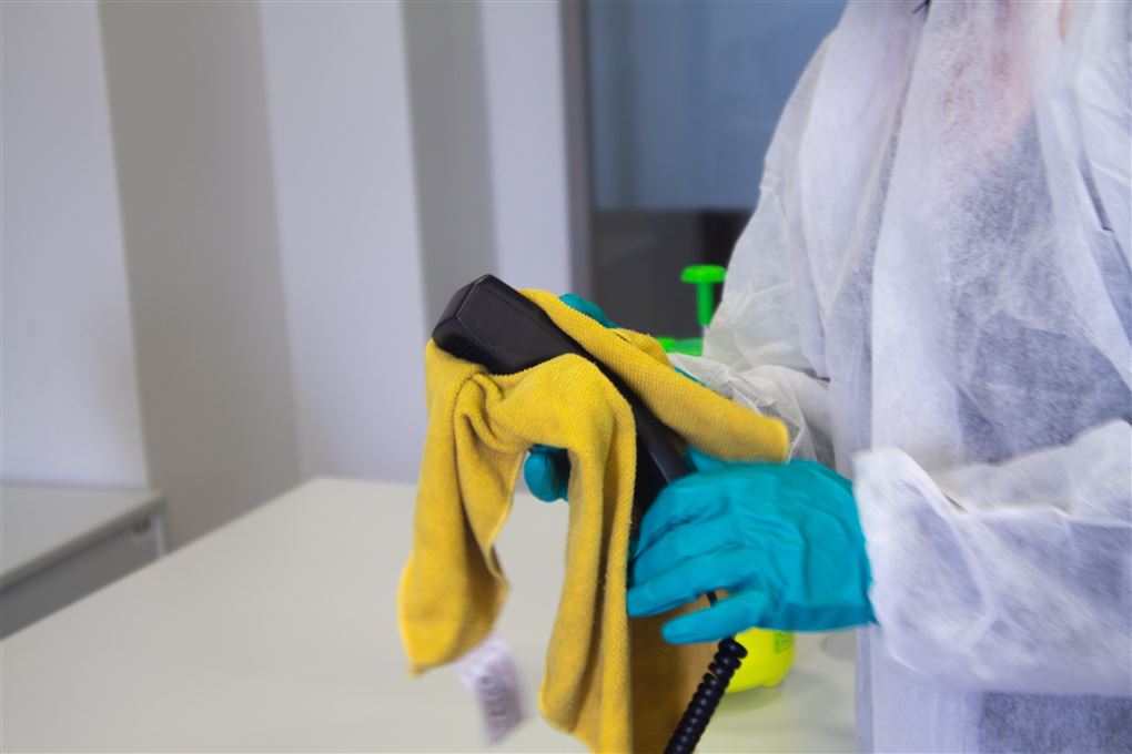 En handskeklædt rengøringsassistent afvasker et telefonrør