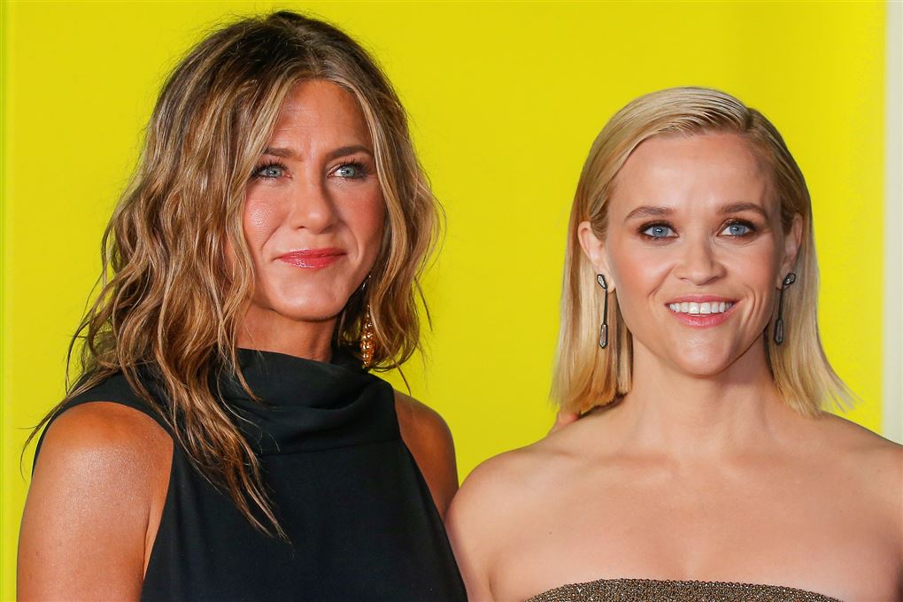 Nærbillede af Jennifer Aniston med løst krøllet hår og Reese Witherspoon med tilbagestrøget løst hår.