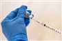 En vaccine dosis trækkes op i en nål. Glasset holdes af en hånd med en blå plastik handske. 