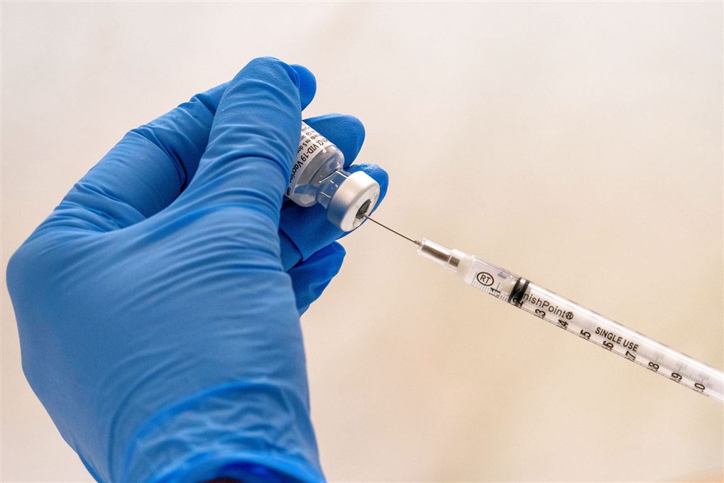 En vaccine dosis trækkes op i en nål. Glasset holdes af en hånd med en blå plastik handske. 